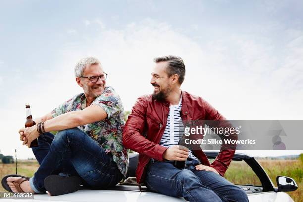 portrait of two mature adult men taking a break from driving sitting on the trunk - altbier stock-fotos und bilder