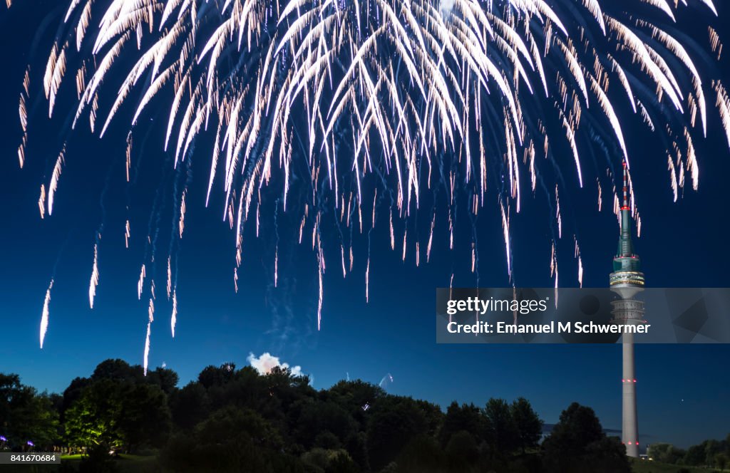 Spectacular, majestic fireworks display with colorful starburst explosives exploding in the night sky, rockets shot up bursting, glowing, sparkling and streaking lights during summer festival with Munich’s . TV Tower in background illuminated