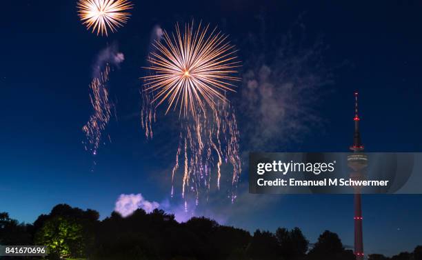 spectacular, majestic fireworks display with colorful starburst explosives exploding in the night sky, rockets shot up bursting, glowing, sparkling and streaking lights during summer festival with munich’s . tv tower in background illuminated - olympiapark stock pictures, royalty-free photos & images