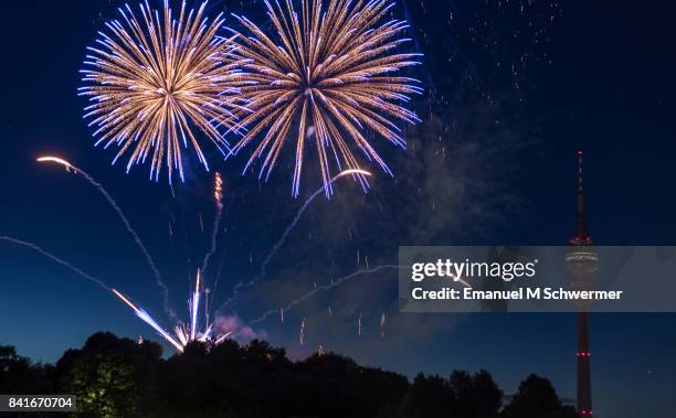 spectacular, majestic fireworks display with colorful starburst explosives exploding in the night sky, rockets shot up bursting, glowing, sparkling and streaking lights during summer festival with munich’s . tv tower in background illuminated - olympiaturm stock-fotos und bilder