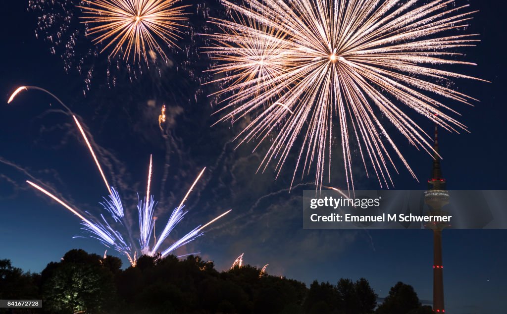 Spectacular, majestic fireworks display with colorful starburst explosives exploding in the night sky, rockets shot up bursting, glowing, sparkling and streaking lights during summer festival with Munich’s . TV Tower in background illuminated