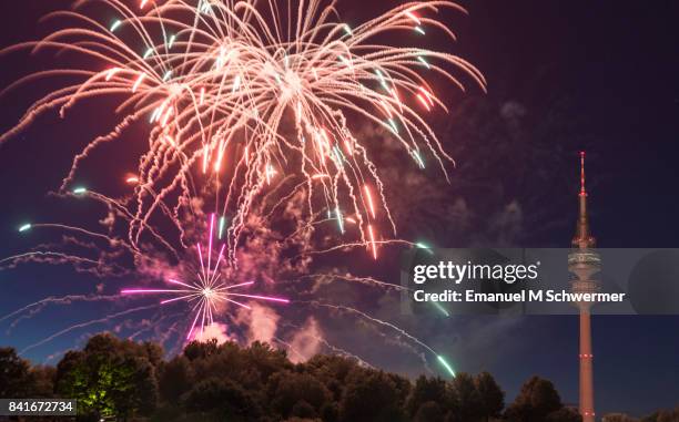 spectacular, majestic fireworks display with colorful starburst explosives exploding in the night sky, rockets shot up bursting, glowing, sparkling and streaking lights during summer festival with munich’s . tv tower in background illuminated - olympiaturm stock-fotos und bilder