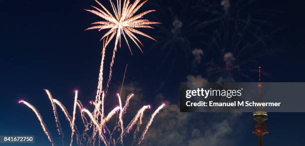 spectacular, majestic fireworks display with colorful starburst explosives exploding in the night sky, rockets shot up bursting, glowing, sparkling and streaking lights during summer festival with munich’s . tv tower in background illuminated - olympiaturm stock-fotos und bilder