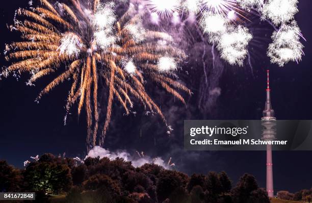 finale of spectacular, majestic fireworks display with colorful starburst explosives exploding in the night sky, rockets shot up bursting, glowing, sparkling and streaking lights during summer festival, munich’s olympic tv tower in background illuminated - olympiaturm stock-fotos und bilder