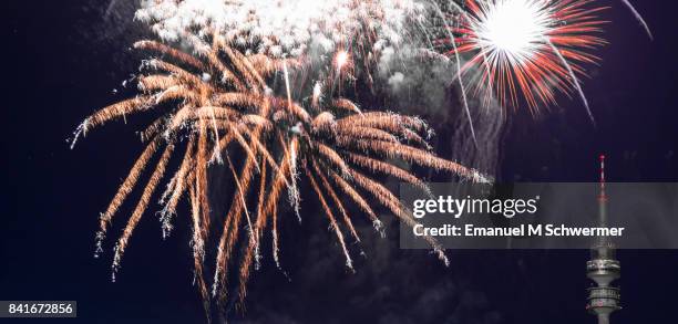spectacular, majestic fireworks display with colorful starburst explosives exploding in the night sky, rockets shot up bursting, glowing, sparkling and streaking lights during summer festival with munich’s . tv tower in background illuminated - olympiaturm stock-fotos und bilder