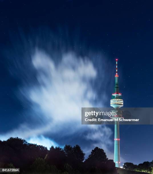 wide shot of munich’s . tv tower in . park illuminated during night with blue night sky and smoke cloud - olympiaturm stock-fotos und bilder