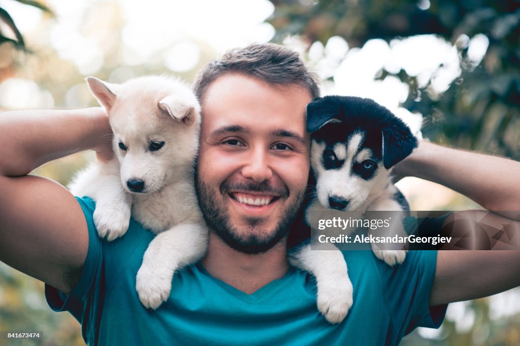 Alegre joven hombre sostiene dos hermosos Husky bebé Puppies