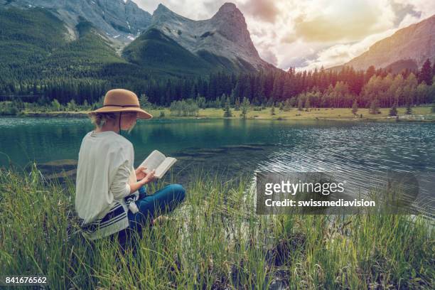 giovane donna che legge un libro sul lago - idyllic lake foto e immagini stock