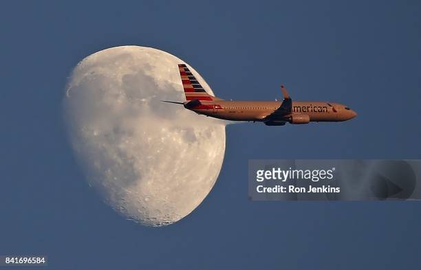 An American Airlines jetliner flies past the moon as the Los Angeles Angels of Anaheim play the Texas Rangers during the first inning at Globe Life...
