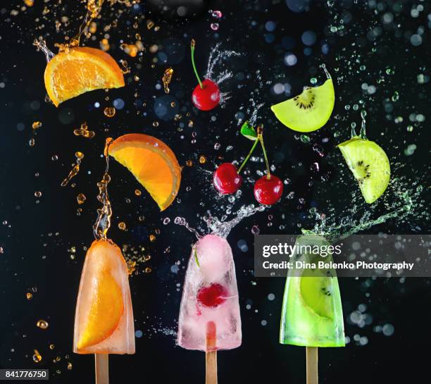 popsicles with fresh cherries, orange slices and kiwi fruit on a dark background, dynamic shot with action, splash, water drops and bokeh. - flying kiwi stock pictures, royalty-free photos & images