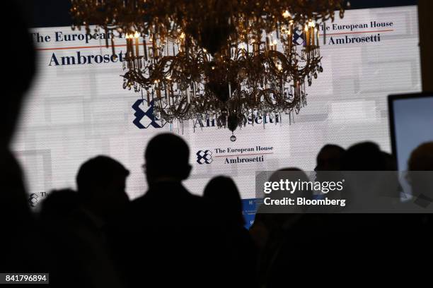 Attendees stand silhouetted against an information screen during the Ambrosetti Forum in Cernobbio, Italy, on Saturday, Sept. 2, 2017. Policy makers...