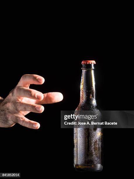 bottle of beer with the glass esmerilado with drops of water and the hands of a man grab  on a black background - beer mat stockfoto's en -beelden