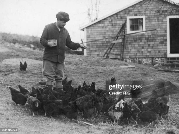 American baseball player Babe Ruth feeds chickens on his farm during the off-season, Sudbury, Massachusetts, 1923.