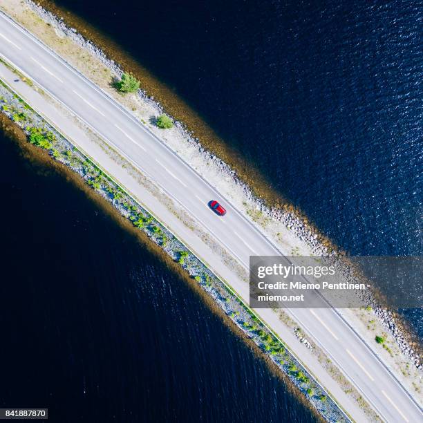 top-down aerial view into a solitary car driving on a narrow ridge road crossing lake päijänne in finland - car top down stock pictures, royalty-free photos & images