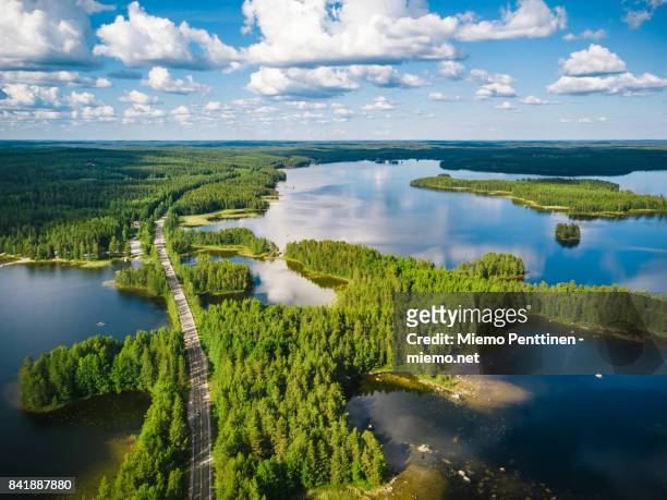 aerial view of a winding road passing through forests & lakes in finland on a summer day - finnland stock-fotos und bilder