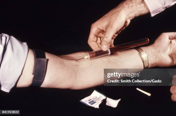 The CDC clinician shown here is using a Vacutainer to obtain a blood sample during an arbovirus study, 1974. Image courtesy CDC. .