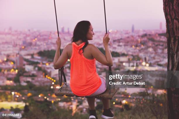 beautiful woman enjoying a unique swing on a tree on top of barcelona mountain contemplating the city at sunset with elevated point of view during summer good vibes in a romantic place. - woman on swing stock pictures, royalty-free photos & images