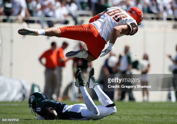 Hunter Folkertsma of the Bowling Green Falcons flies over the tackle of David Dowell of the Michigan State Spartans at Spartan Stadium on September...