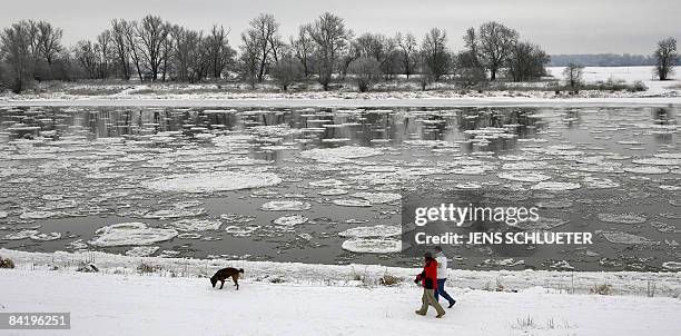 Couple walks their dog along the snow covered banks of the Elbe river on which float sheets of ice on January 7, 2009 in the eastern town of Dessau,...