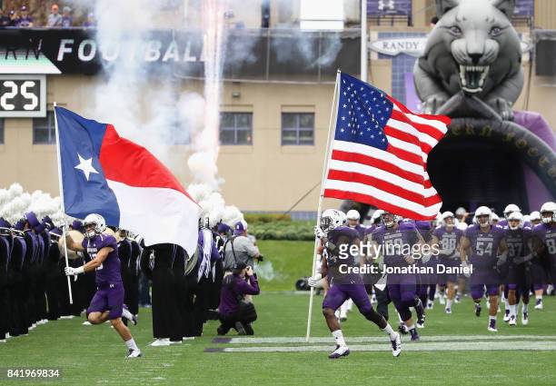 Macan Wilson of the Northwestern Wildcats runs on to the field with the state flag of Texas as teammate Montre Hartage carries the American flag...