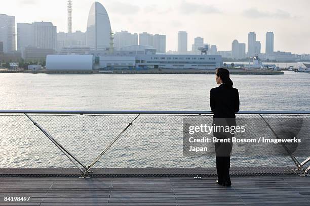 japan, kanagawa prefecture, yokohama city, business woman standing by river, skyline in background, rear view - yokohama skyline stock pictures, royalty-free photos & images