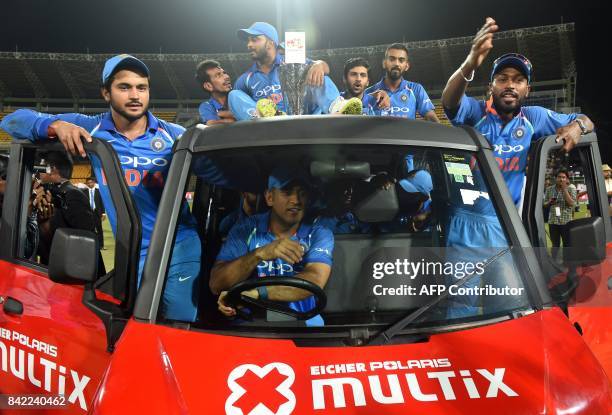 Indian cricketer Mahendra Singh Dhoni rides a vehicle carrying fellow team members and the winning trophy after their win over Sri Lanka in the fifth...