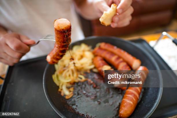 man eating sausages, close-up for breakfast on hot electric hob - carne procesada fotografías e imágenes de stock