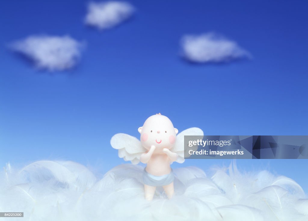 Doll with angel's wings standing on feathers