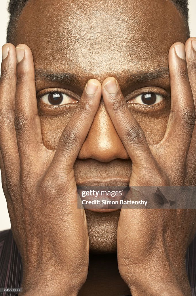 Man with hands covering face, eyes showing