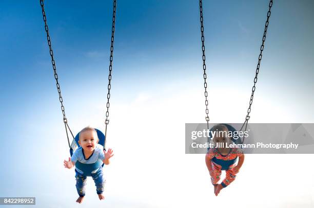 12 month old fraternal boys swing in pajamas at a park - fraternal twin stock pictures, royalty-free photos & images