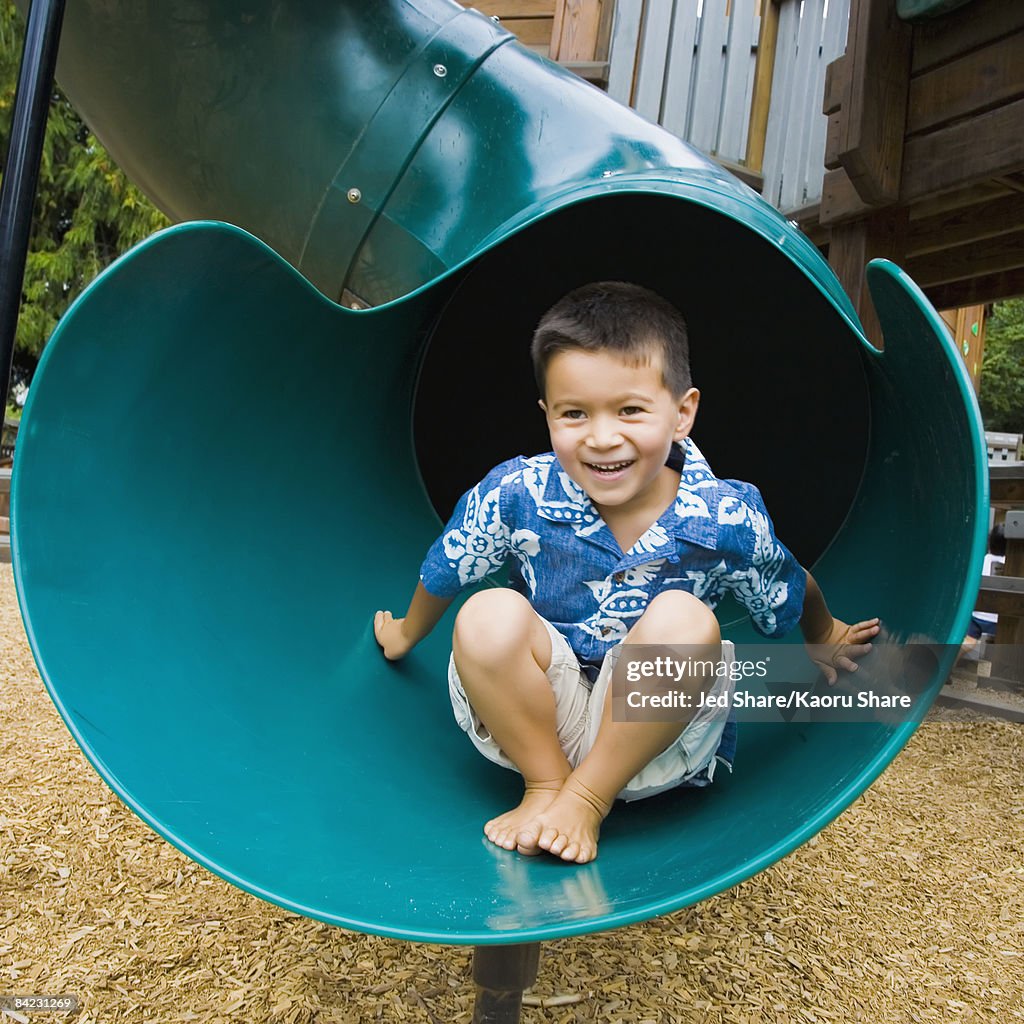 Mixed race boy sliding down slide in playground - Stock Photo
