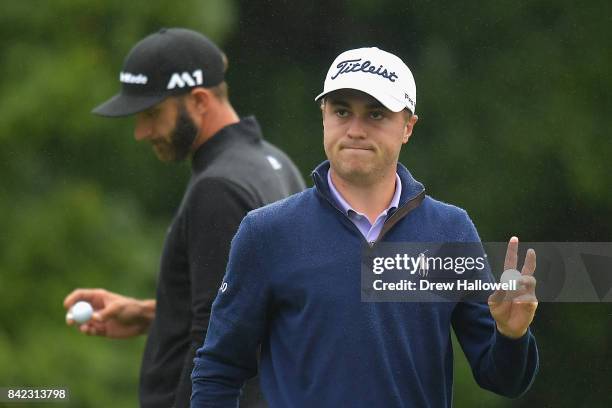 Justin Thomas of the United States acknowledges fans after putting on the 18th green as Dustin Johnson of the United States looks on during round...