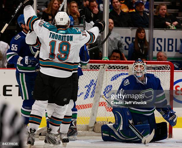 Joe Thornton of the San Jose Sharks lifts his arms celebrating a Sharks goal while Curtis Sanford of the Vancouver Canucks looks up dejected during...