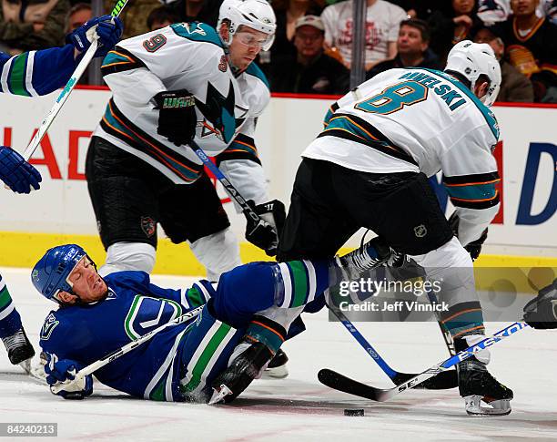 Ryan Johnson of the Vancouver Canucks is knocked to the ice in front of Joe Pavelski of the San Jose Sharks and teammate Milan Michalek during their...