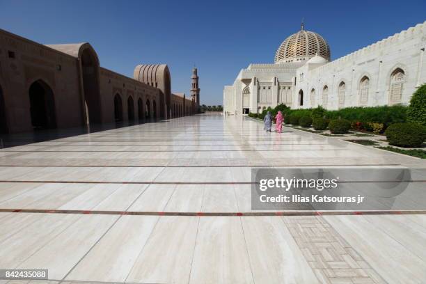 ourists covered in colorful garments walk along the exterior courtyard of the sultan qaboos grand mosque, in musqat, oman - grand mosque oman stock-fotos und bilder