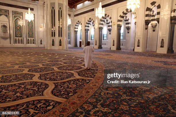 an omani in traditional dress stepping on persian carpet in the main prayer hall of the sultan qaboos grand mosque, muscat, oman - sultan qaboos grand mosque stock pictures, royalty-free photos & images