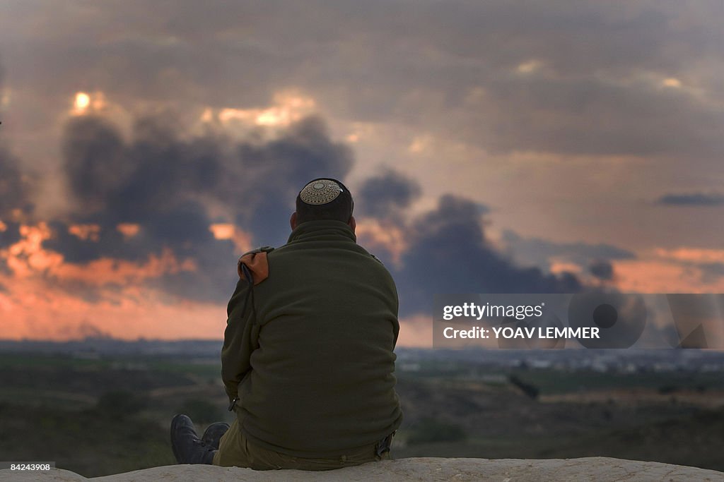 An Israeli soldier watches smoke billowi