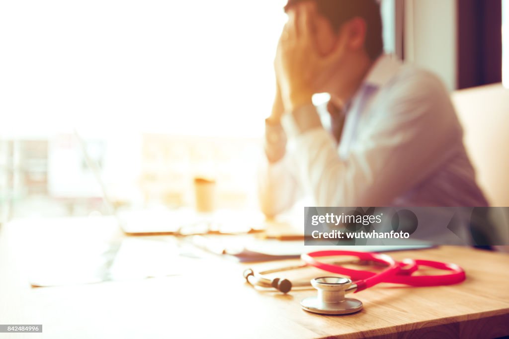Close up stethoscope and asian doctor sitting with laptop with stress headache.