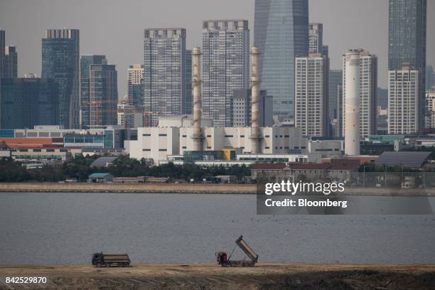 Trucks sit parked on a port construction site as skyscrapers and high-rise buildings stand in the background in the Songdo district of Incheon, South...