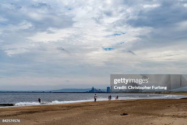People walk on the beach of Seaton Carew with the now closed Redcar Coking plant in the distance on September 4, 2017 in Hartlepool, England....