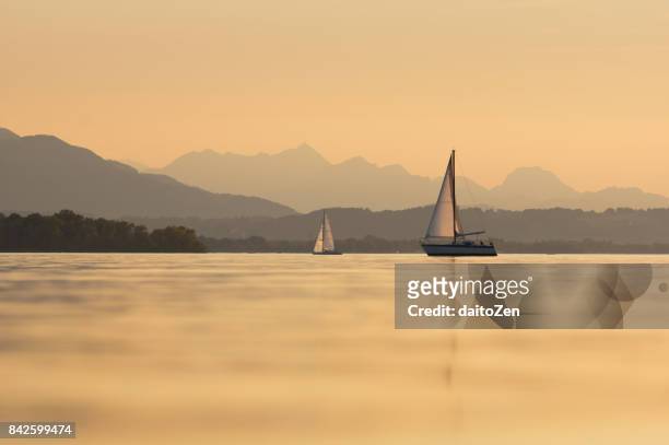 two sailboats on lake chiemsee, hochries and wendelstein mountains in the background, upper bavaria, germany - chiemsee stockfoto's en -beelden