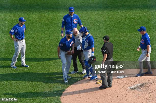 Jake Arrieta of the Chicago Cubs grabs his leg as he is looked at by Assistant Athletic Trainer Ed Halbur after an apparent injury in the third...