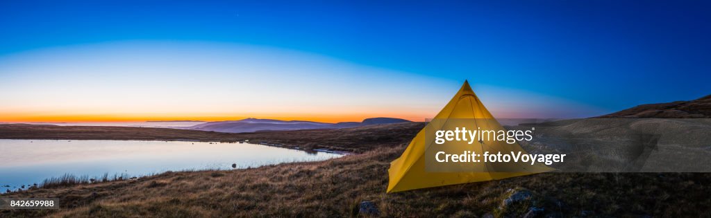 Yellow pyramid tent illuminated sunrise in idyllic mountain wilderness panorama