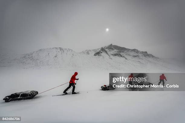 Expedition members ski over the frozen landscape in a blizzard, while towing sleds, during a ski traverse of Akshayuk Pass, in Auyuittuq National...