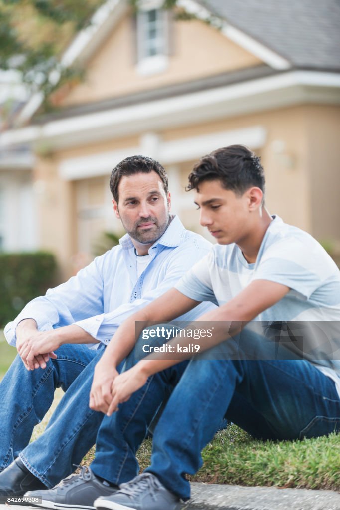 Father sitting with serious teenage boy