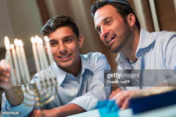 father and teenage son lighting menorah - jewish people stock pictures, royalty-free photos & images