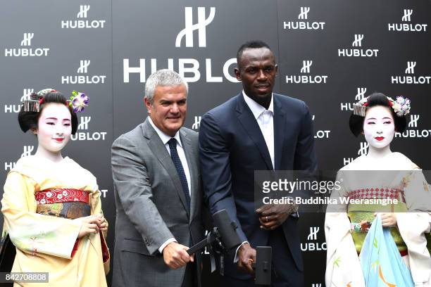 Retired sprinter Usain Bolt and Hublot Executive Director Ricardo Guadalupe pose with geisha girls as they open a sake barrel during the opening...