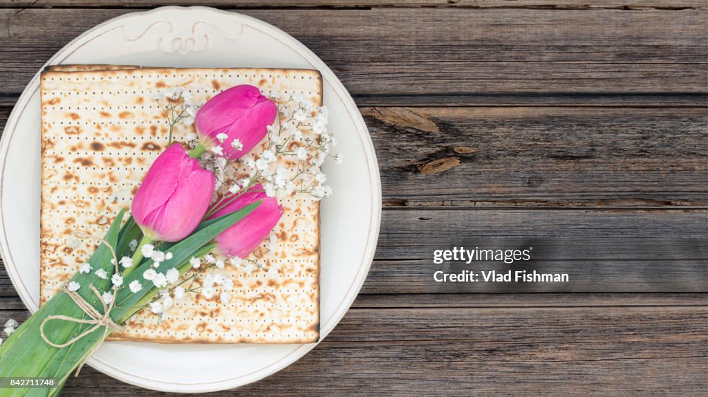 Matzah or matza on a white plate and a tulip flowers on a vintage wood background with copy space.