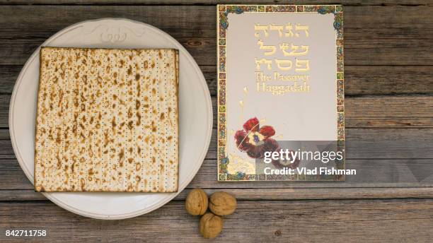 white plate  with matzah or matza and passover haggadah on a vintage wood background presented as a passover seder feast or meal with copy space - matzah stock-fotos und bilder