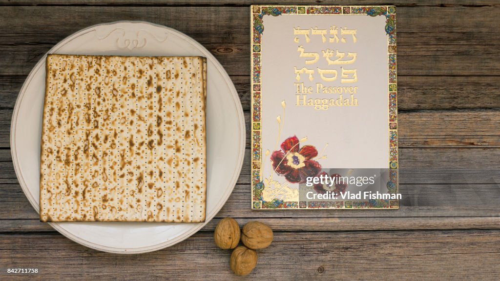 White plate  with matzah or matza and Passover Haggadah on a vintage wood background presented as a Passover seder feast or meal with copy space